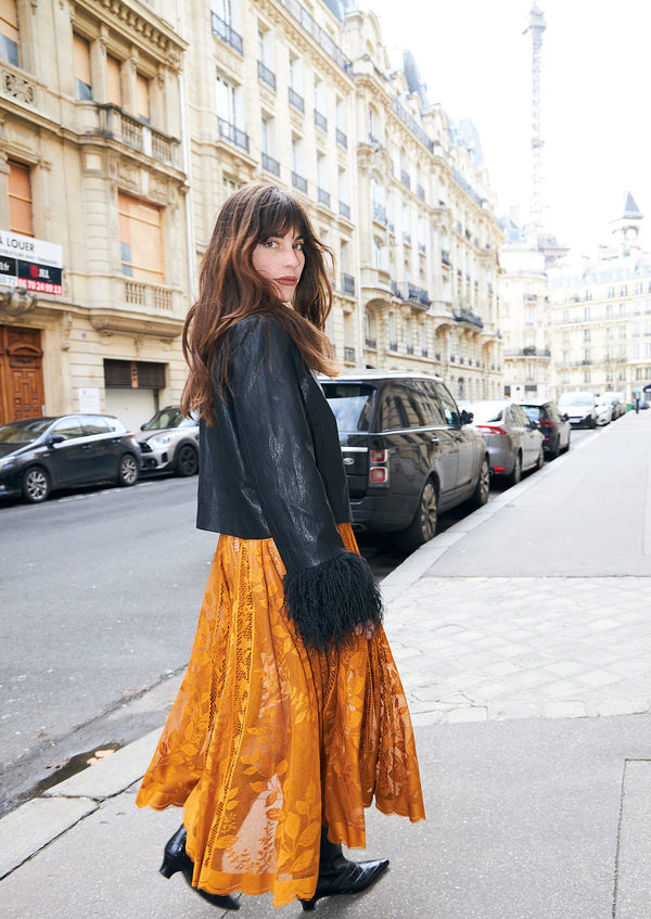 Kvinde iført sort jakke med pelsdetaljer og lang orange blondenederdel. Et feminint Outfit med kontraster, fotograferet i Paris.
