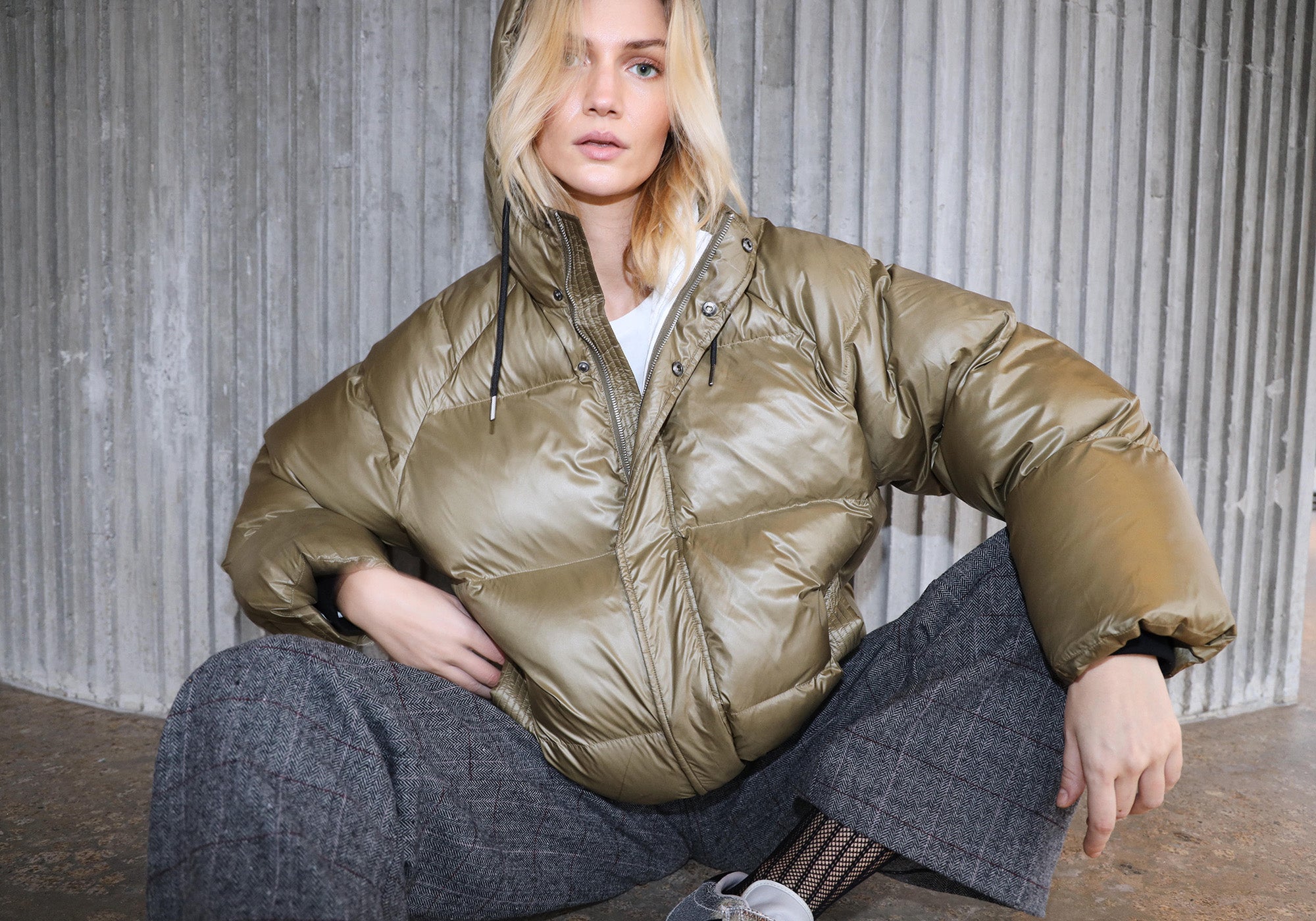 Model iført olivengrøn dunjakke med hætte, stylet med grå ternede bukser og hvid T-shirt fra Lollys Laundry.