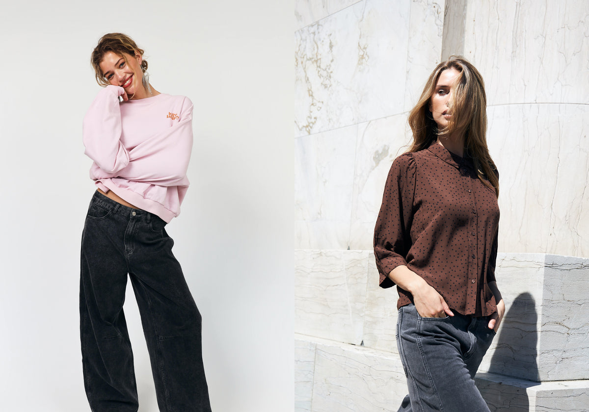 To kvinder i afslappede outfits. Den ene bærer en lyserød sweatshirt med mørkegrå jeans, mens den anden har en brun skjorte med små sorte prikker og grå jeans på.