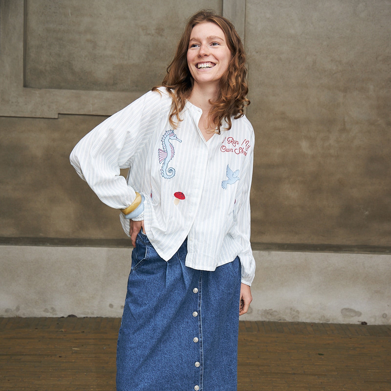 Kvinde iført hvid broderet skjorte med farverige motiver og blå denimnederdel med knapper foran fra Lollys Laundry.