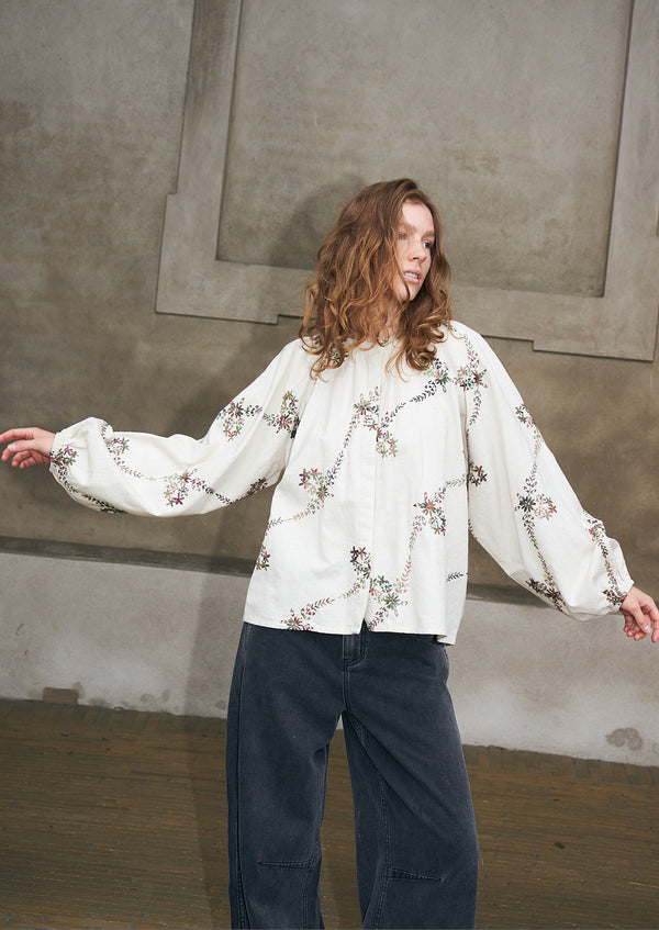 Kvinde iført en cremefarvet bluse med broderede blomstermotiver og mørke denimjeans fra Lollys Laundry.