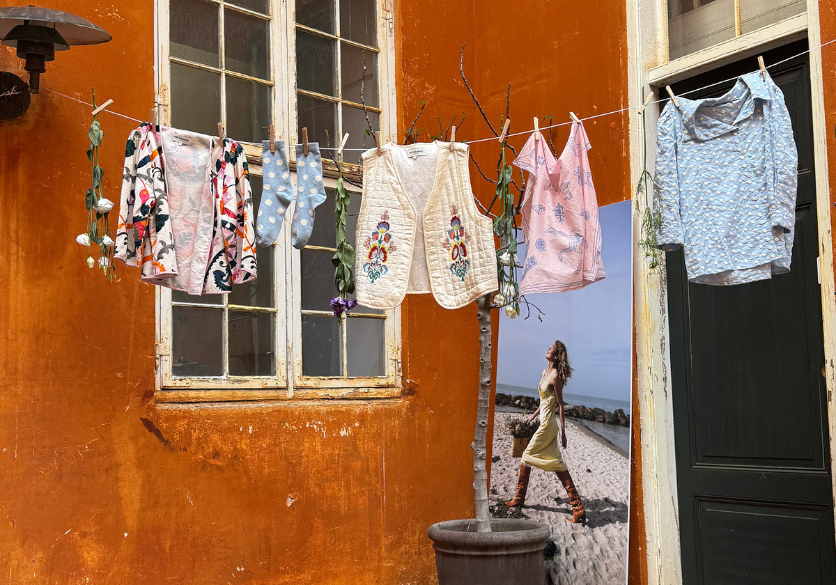 Farverige Lollys Laundry styles og accessories hænger på en tørresnor foran en orange væg i København.